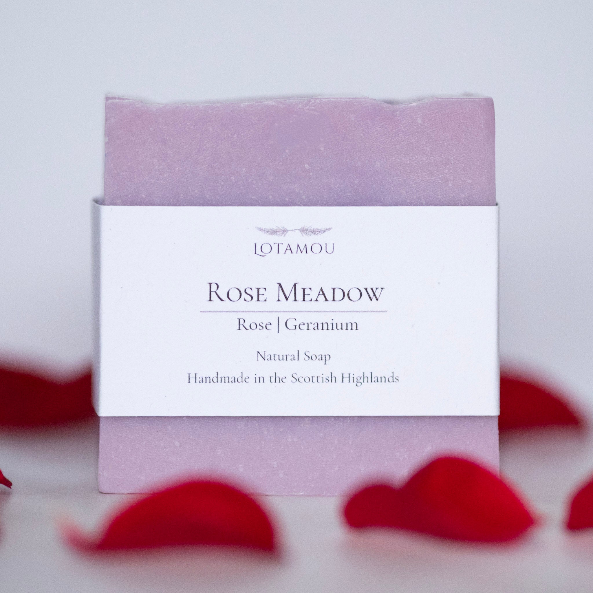 Pink soap bar with a white label on a light background with rose petals