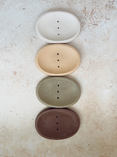 Set of four ceramic soap dishes in different colors on a textured surface