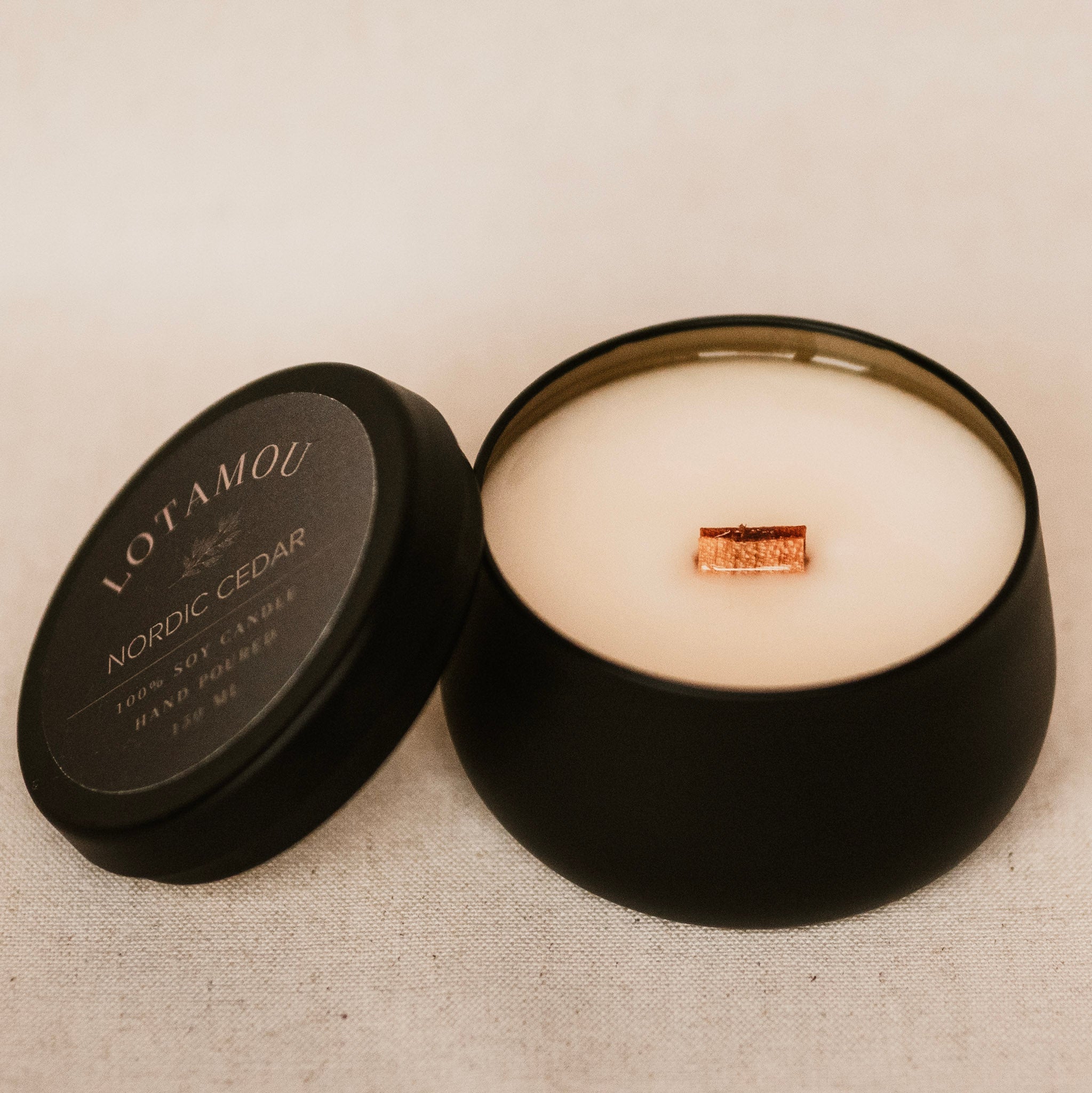 Open black candle container with a candle inside on a textured beige surface
