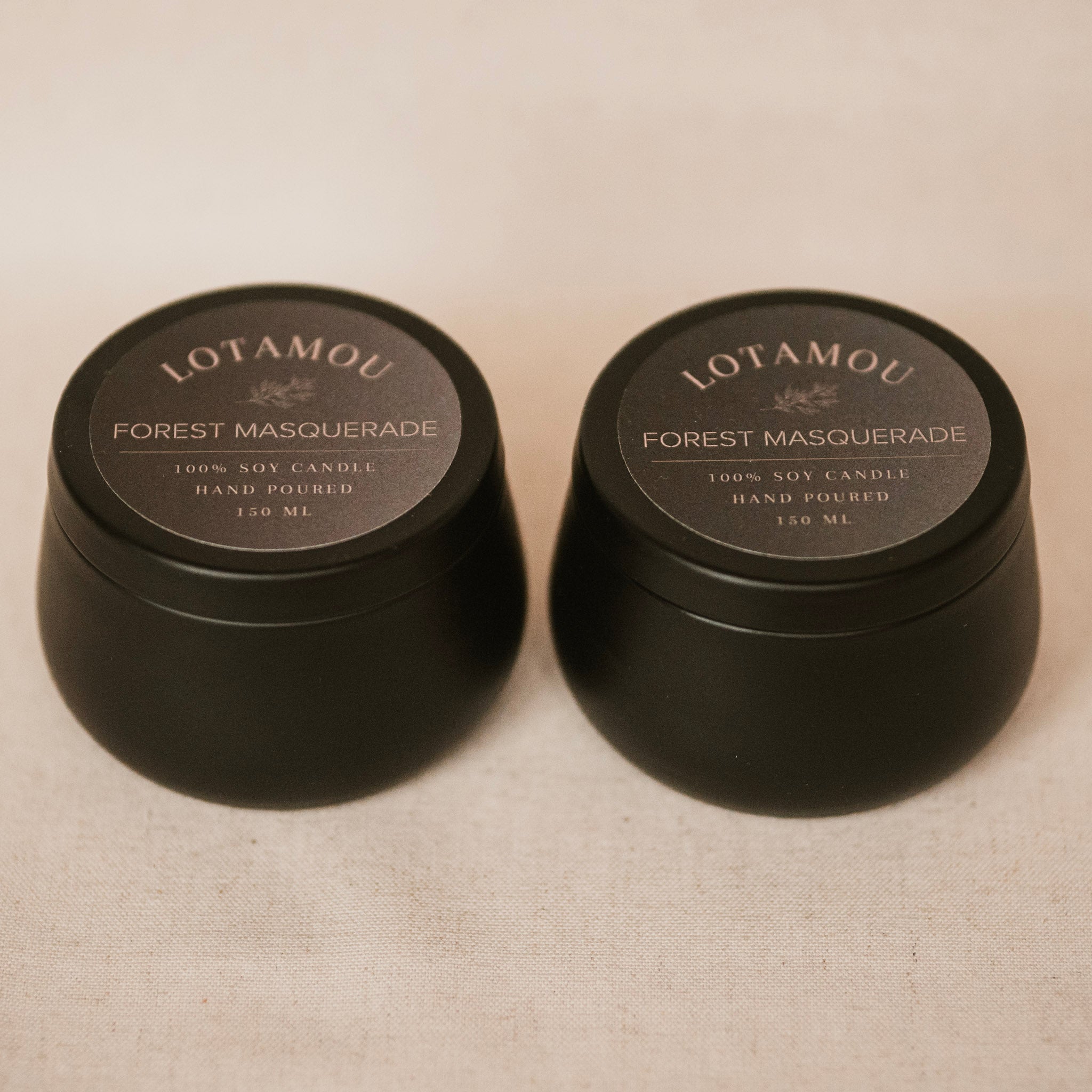 Two black candle containers with 'LOTAMOU' branding on a beige fabric background