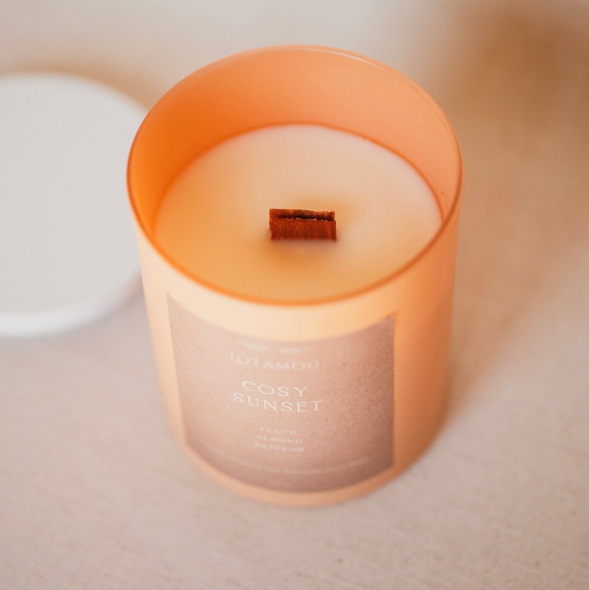 Candle labeled 'Cosy Sunset' with a warm glow on a neutral background