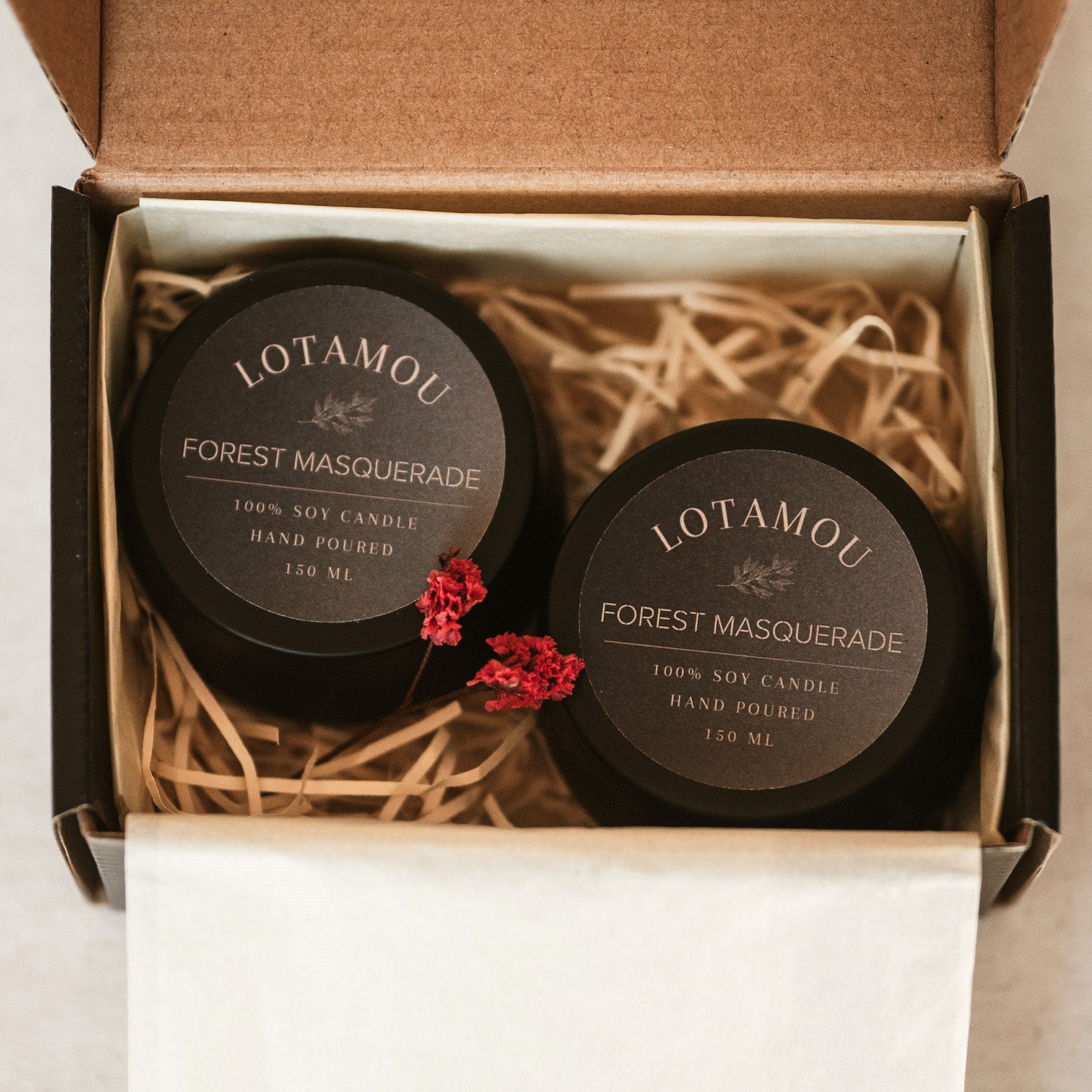 Two Lotamou Forest Masquerade candles in a box with decorative straw and flowers.