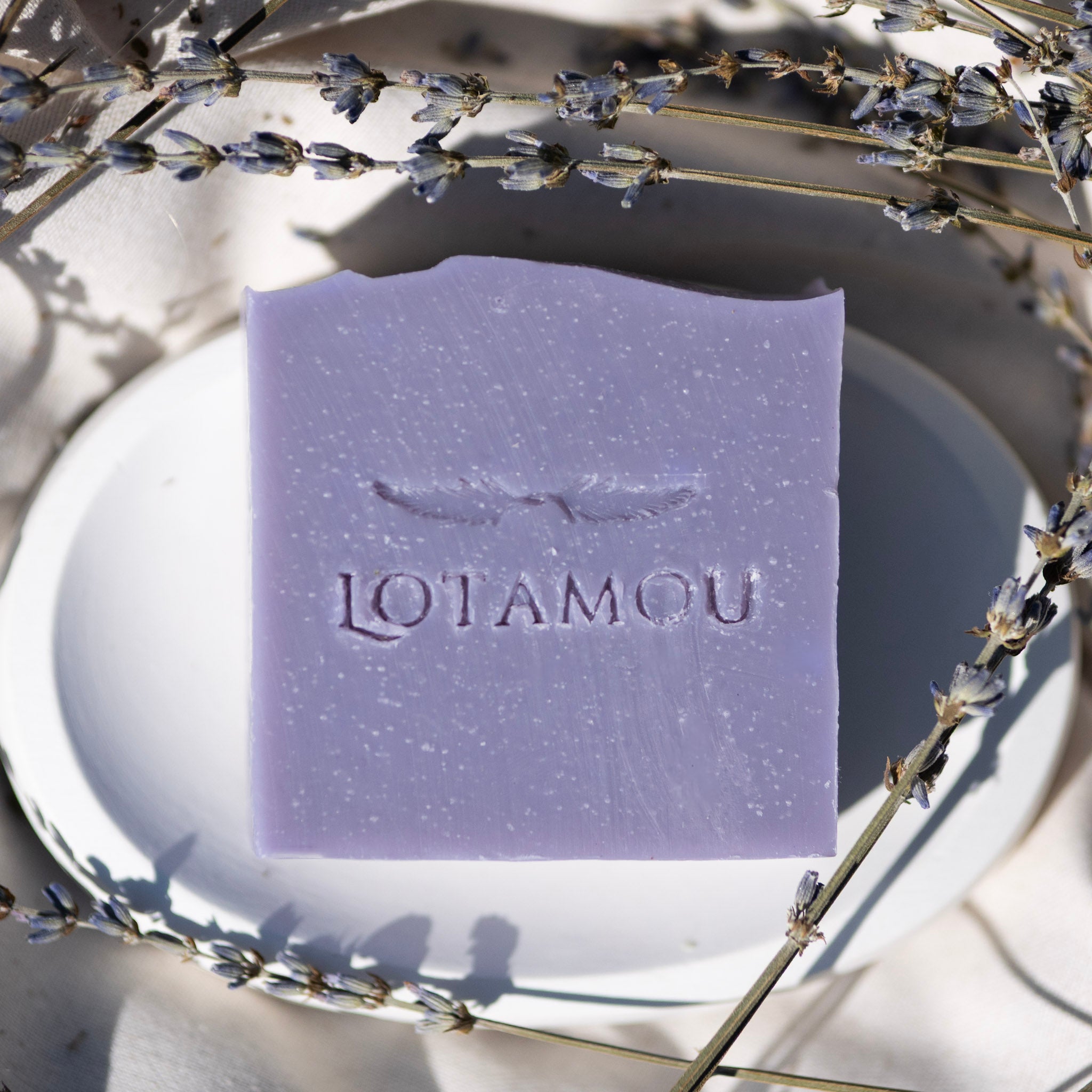 Purple soap bar with 'LOTAMOU' branding on a white plate surrounded by lavender flowers.