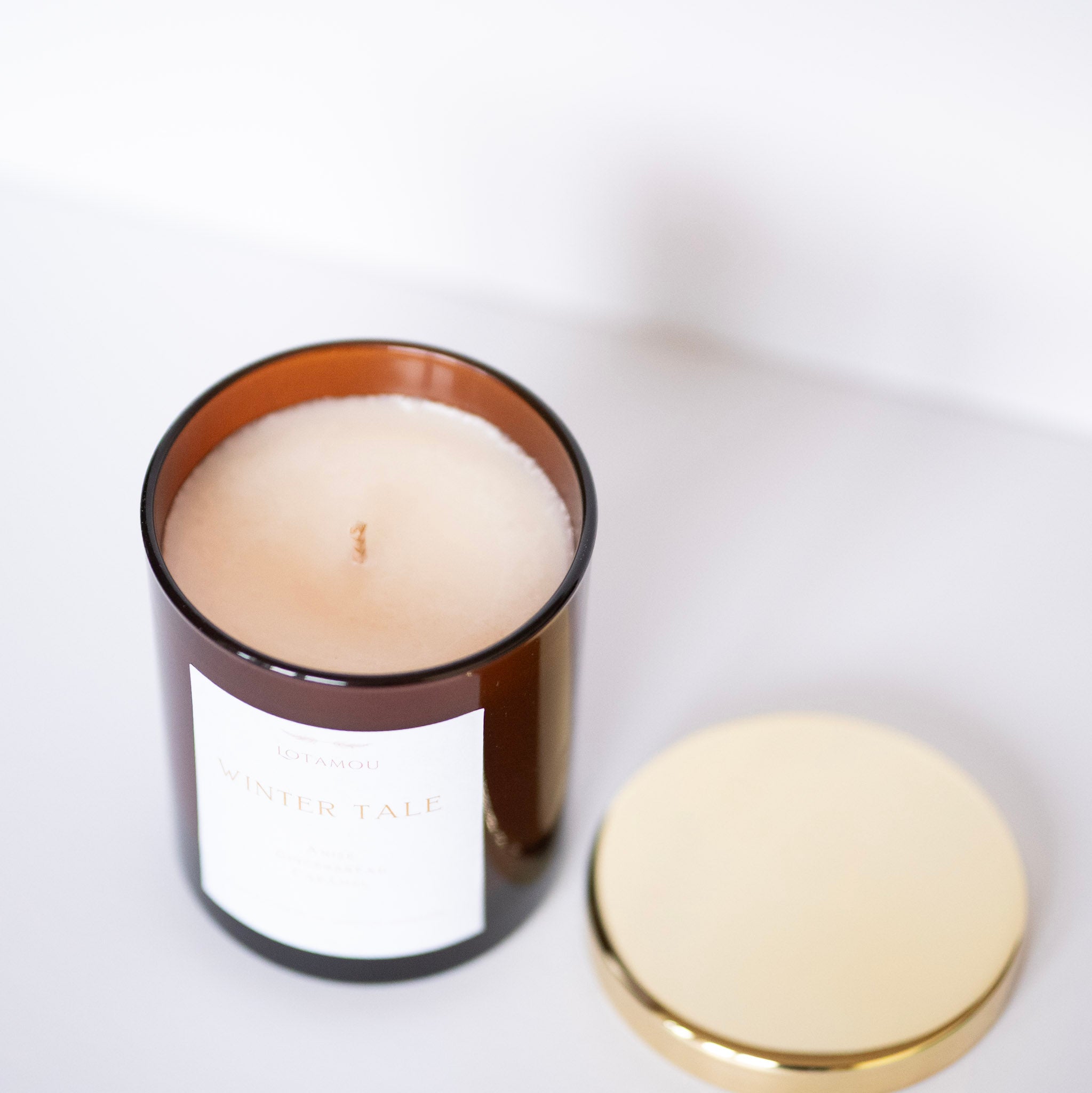 Candle in a brown glass container with a gold lid on a white background