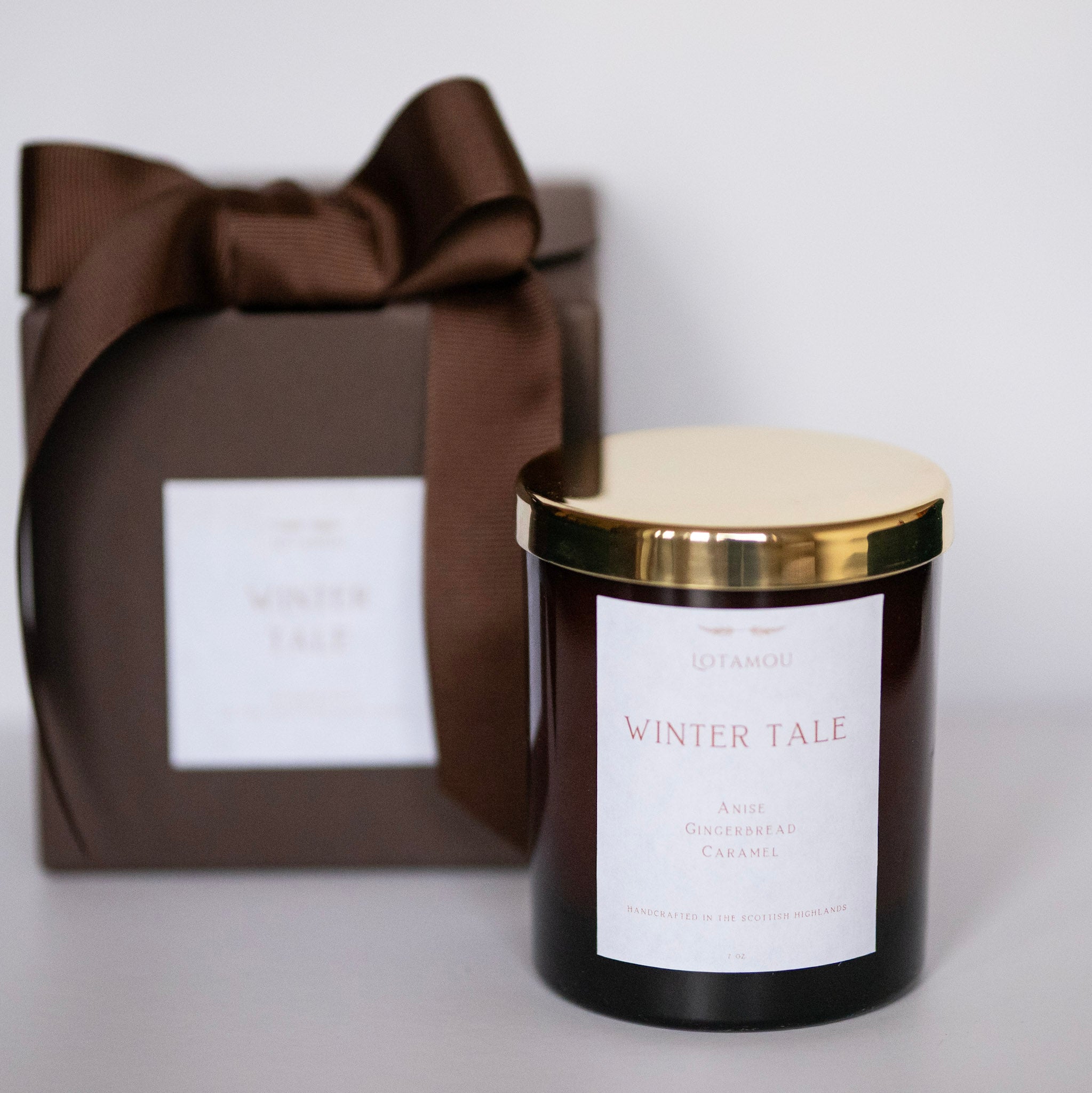 Candle labeled 'Winter Tale' with a brown gift box featuring a bow on a light gray background