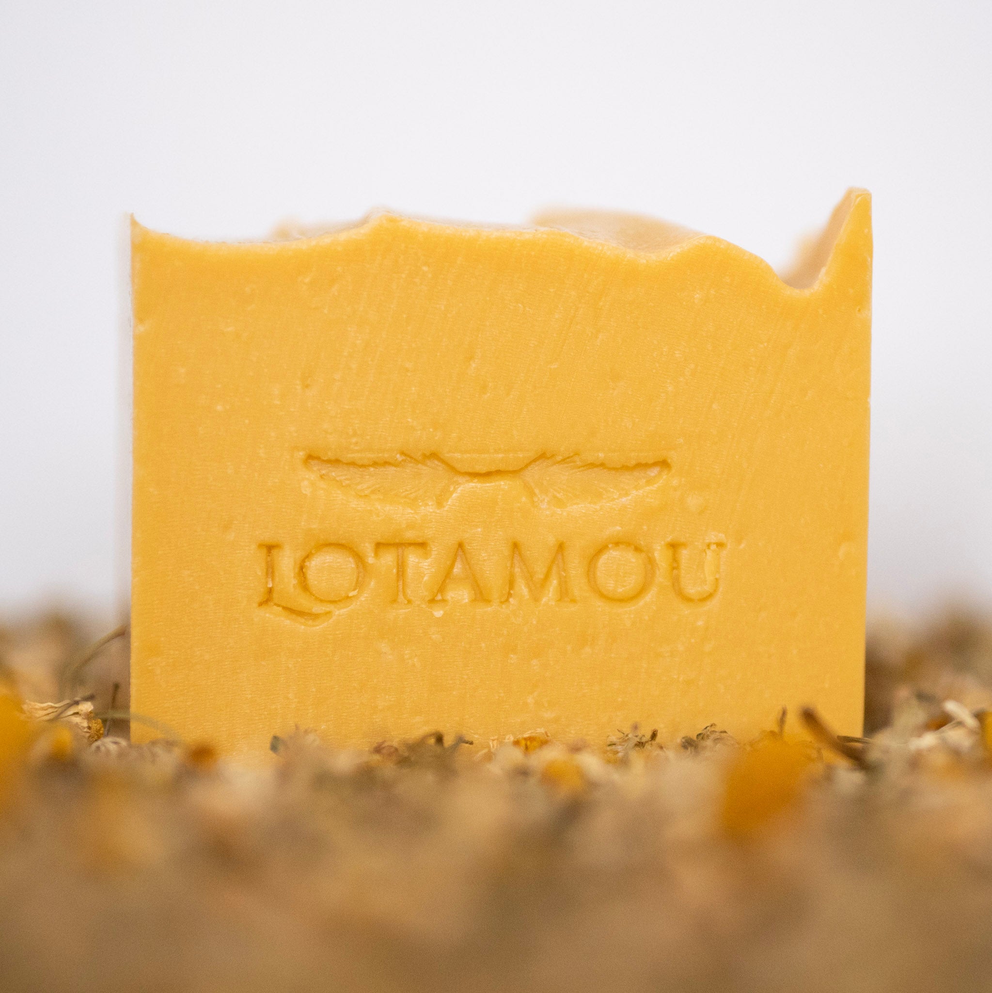 Yellow soap bar with 'LOTAMOU' branding on a blurred natural background