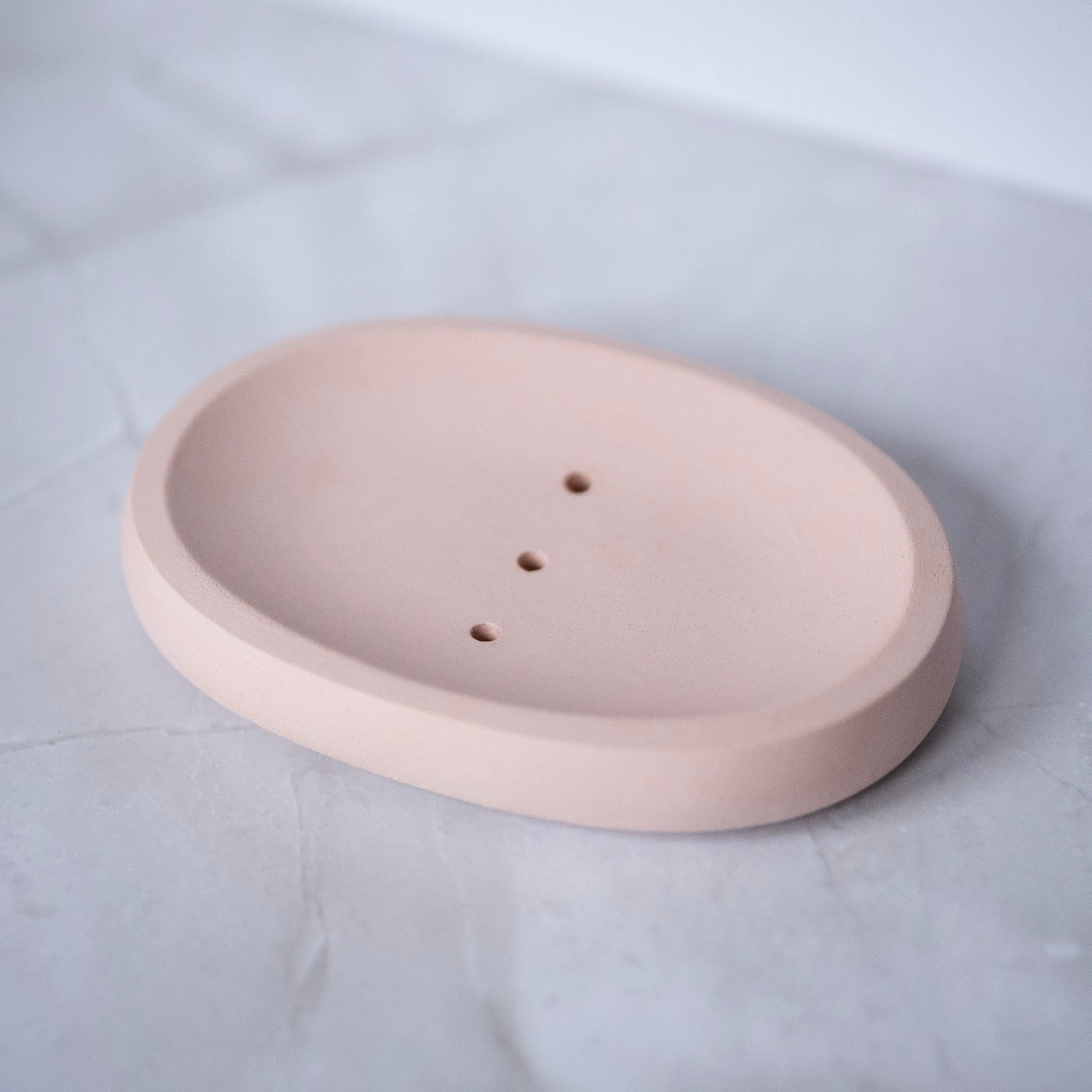 Round beige ceramic plate with three holes on a light gray background