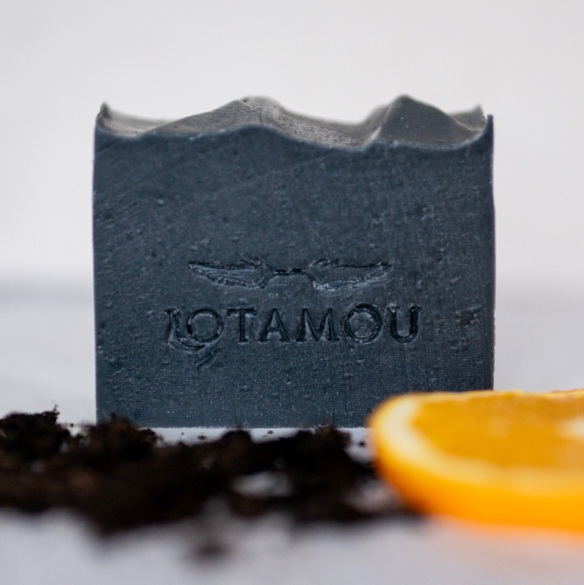Bar of soap with 'LOTAMOU' branding next to an orange slice on a light background
