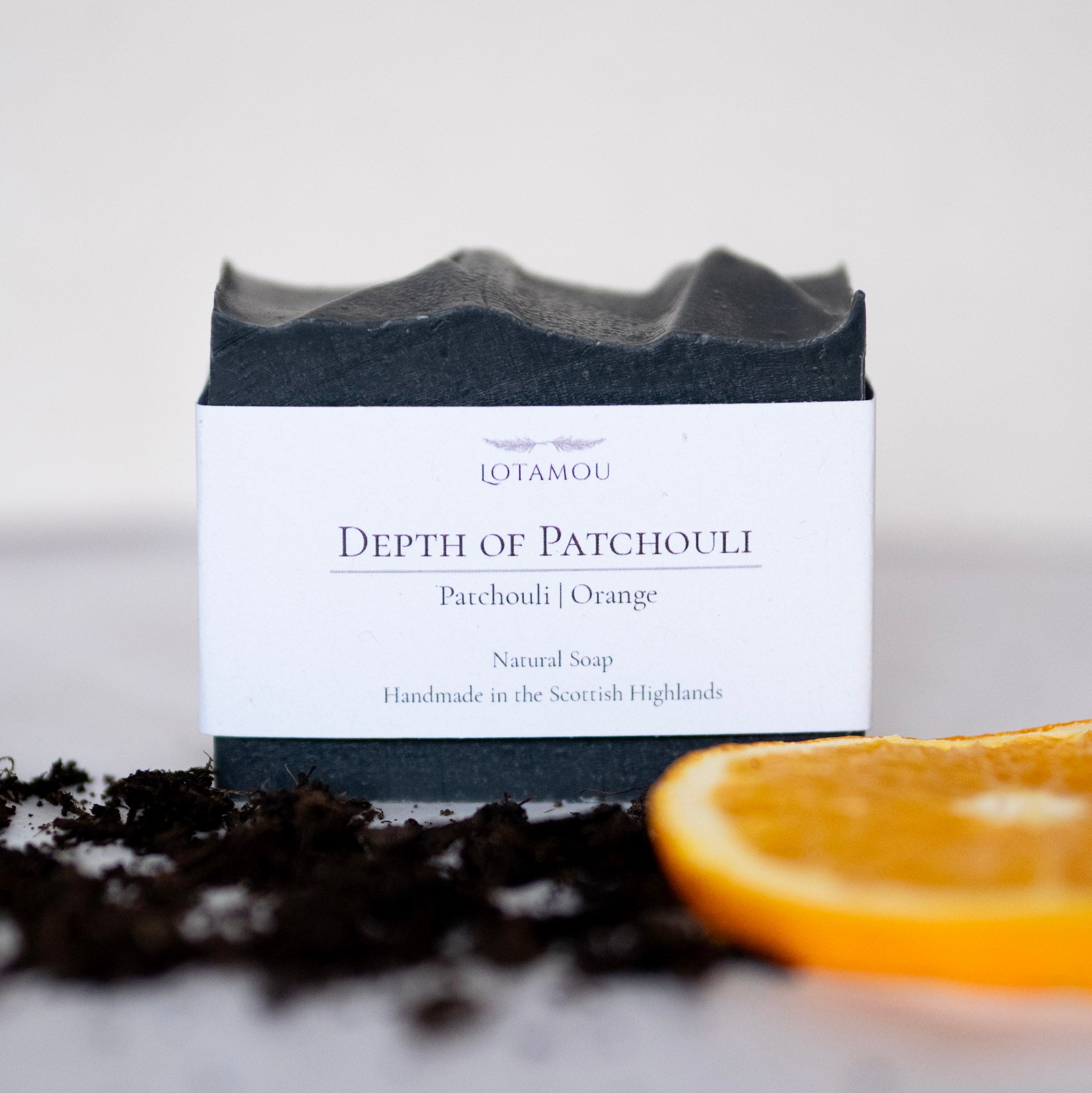 Soap bar with packaging labeled 'Depth of Patchouli' from Lotamou, surrounded by patchouli leaves and an orange slice.