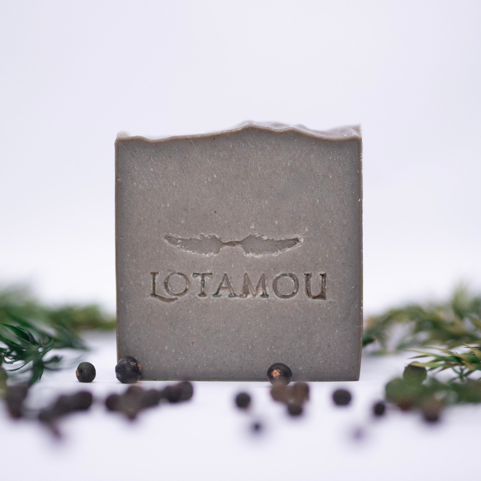 Bar of soap with 'LOTAMOU' branding on a white background with black peppercorns.