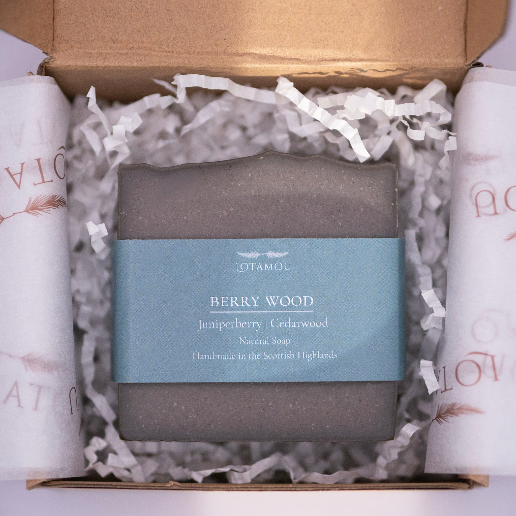 Gray soap bar with blue label in a box with white tissue paper