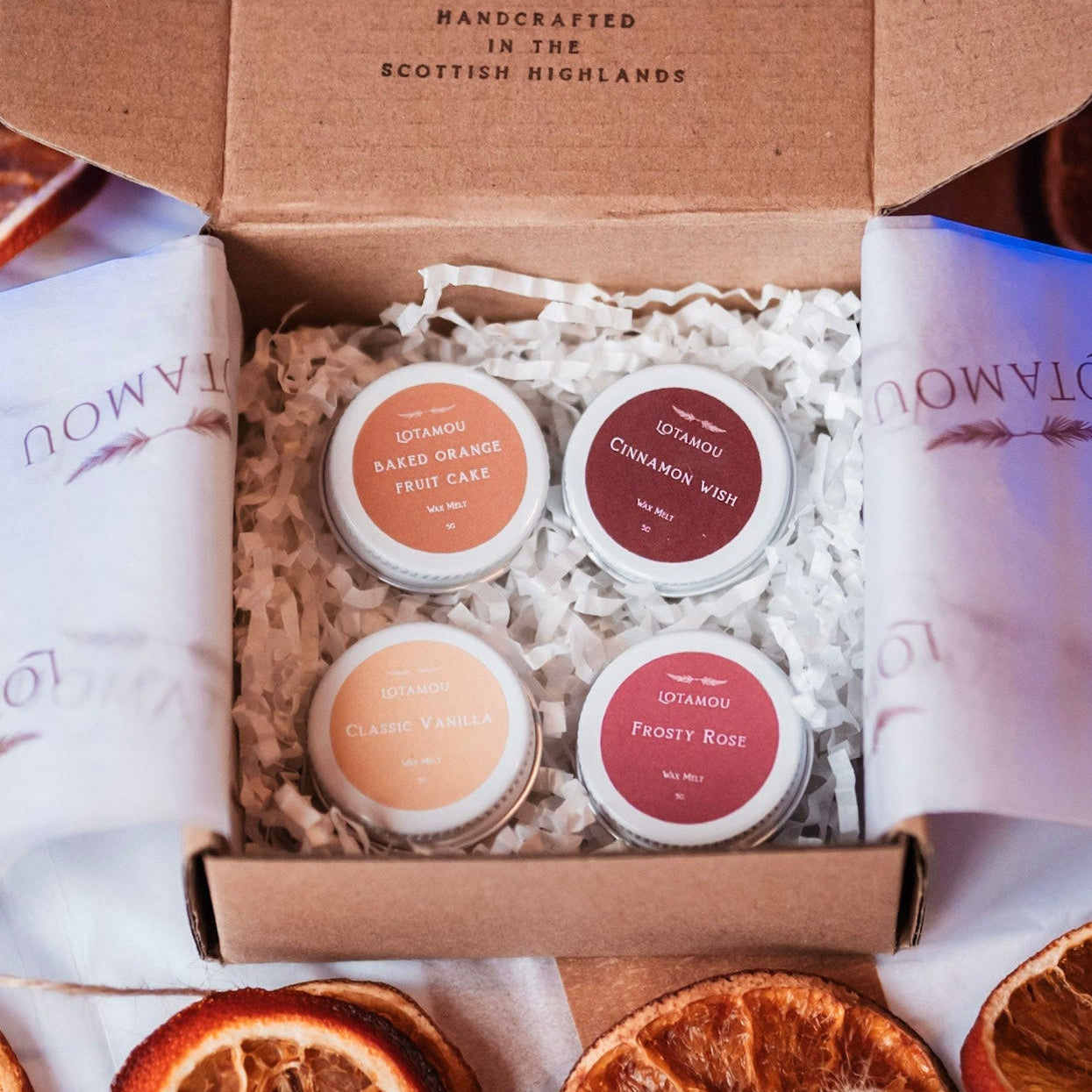 Open box containing Lotamou products with dried oranges on a white surface.