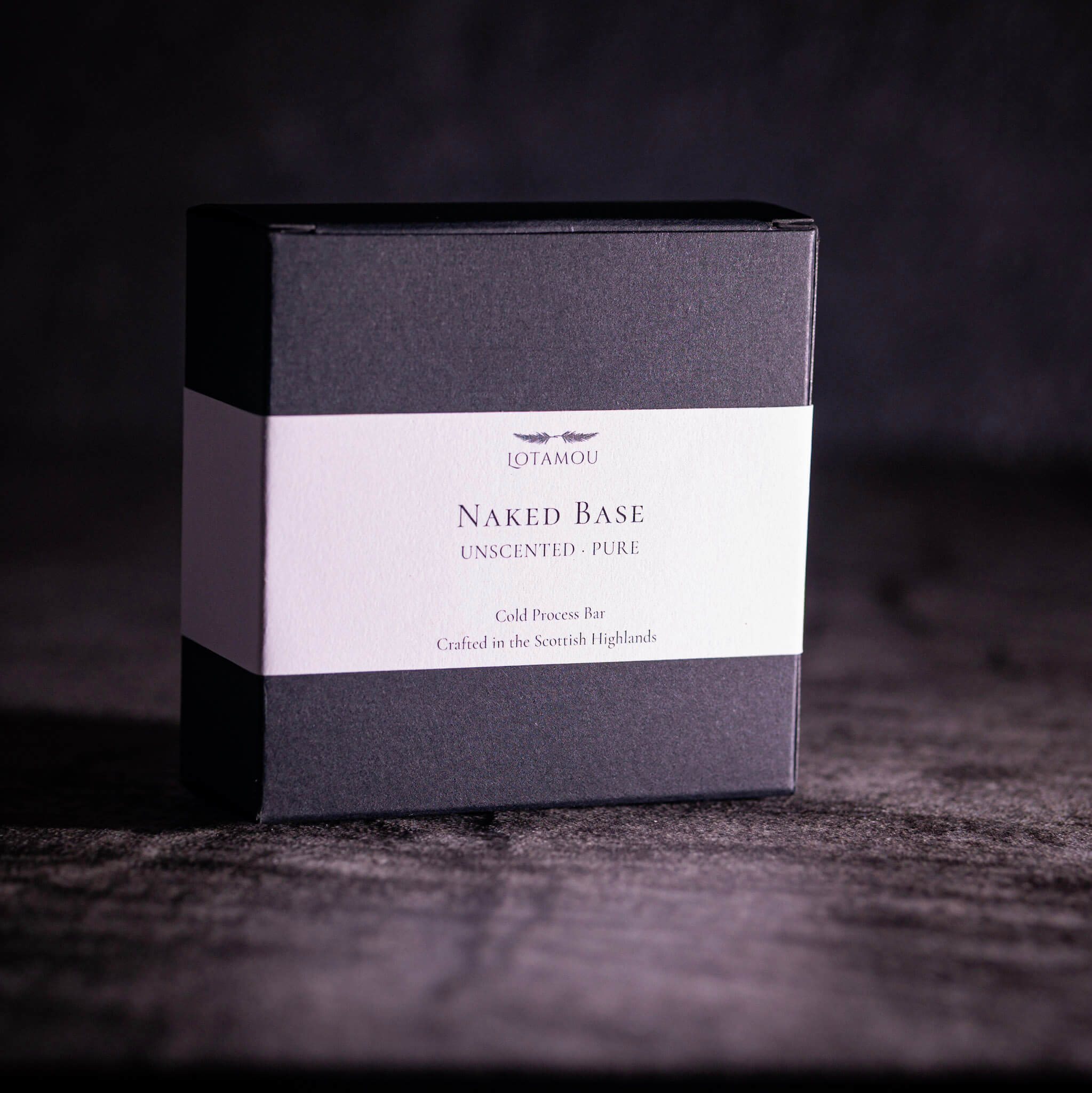 A square dark gray product box with a white label reading 'QIYAMOU Naked Base Unscented - Pure' on a dark textured surface against a dark background.