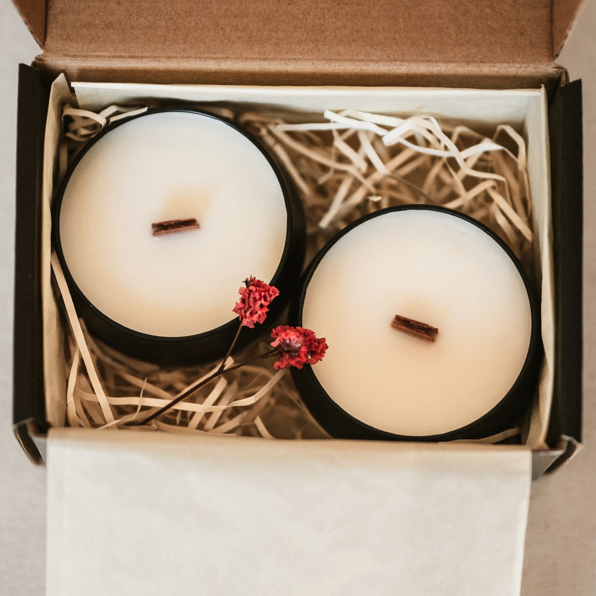 Two candles in a box with straw and red flowers