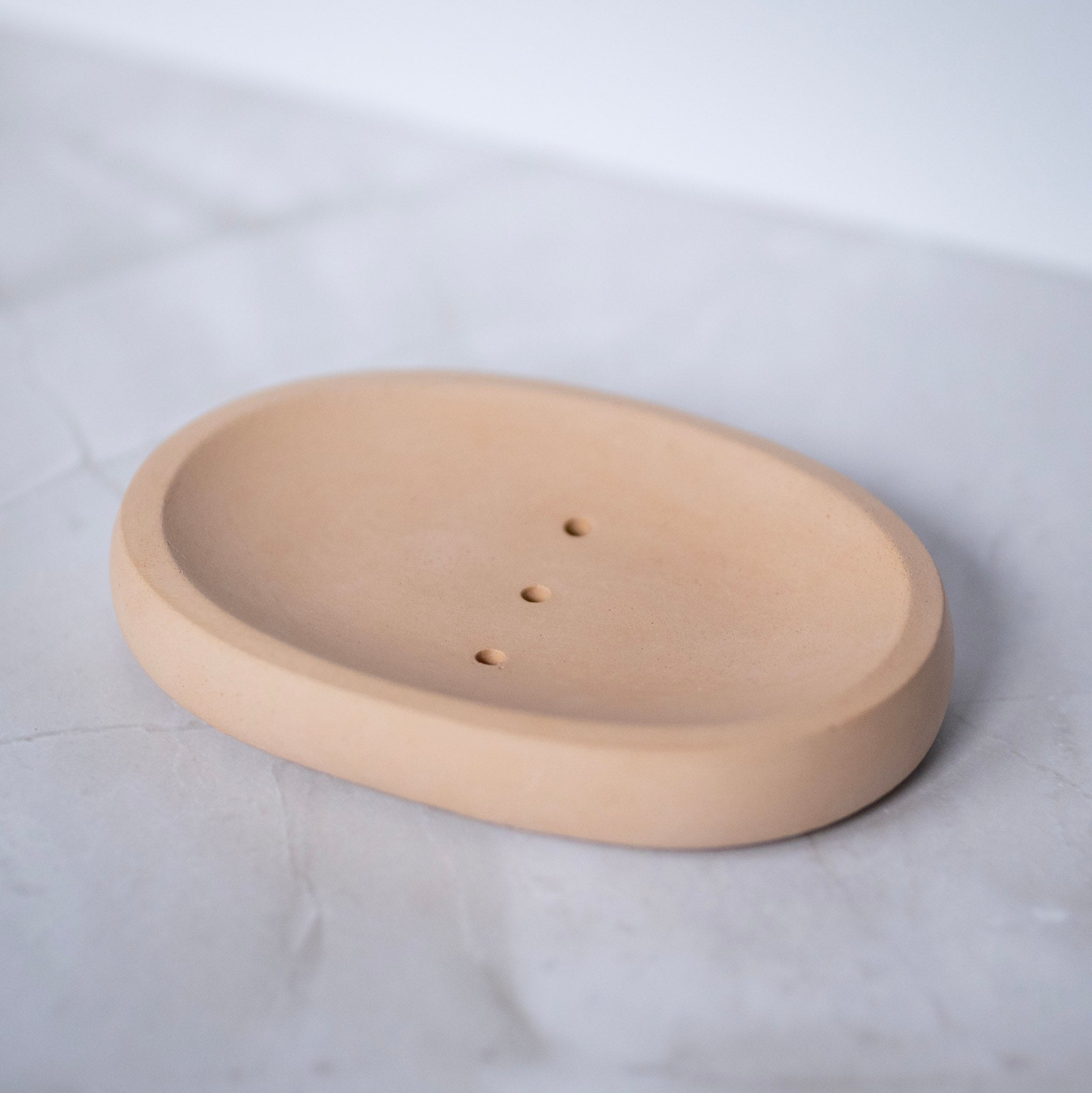 Beige ceramic soap dish on a white marble surface